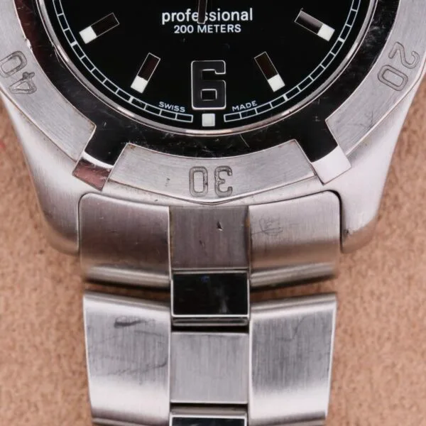 Close-up of a Tag Heuer Professional Dive stainless steel watch with a black dial, featuring professional 200 METERS and SWISS MADE text. It highlights the number 6, silver hour markers, and a robust metal bracelet.