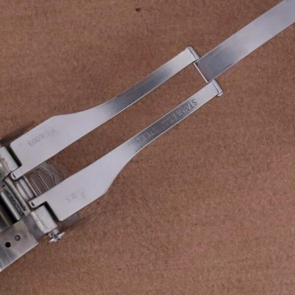 Close-up of a stainless steel hinge on a brown surface, echoing the precision of Tag Heuer Professional Dive watches. The hinge features two parallel arms marked STAINLESS STEEL, highlighting intricate metalwork with visible screws and joints.