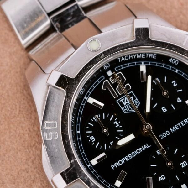 A detailed shot of the Tag Heuer 2000 Professional Chronograph with a metal bracelet; it features a black dial, three sub-dials, silver markers, and a tachymeter scale. It exemplifies precision with water resistance up to 200 meters.