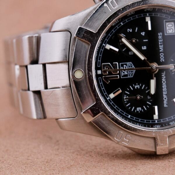 Close-up of a stainless steel Tag Heuer 2000 Professional Chronograph watch featuring a black dial with multiple sub-dials, the logo, and 200 METERS. The time shows approximately 3:20, and the bezel highlights a prominent 50 marking.