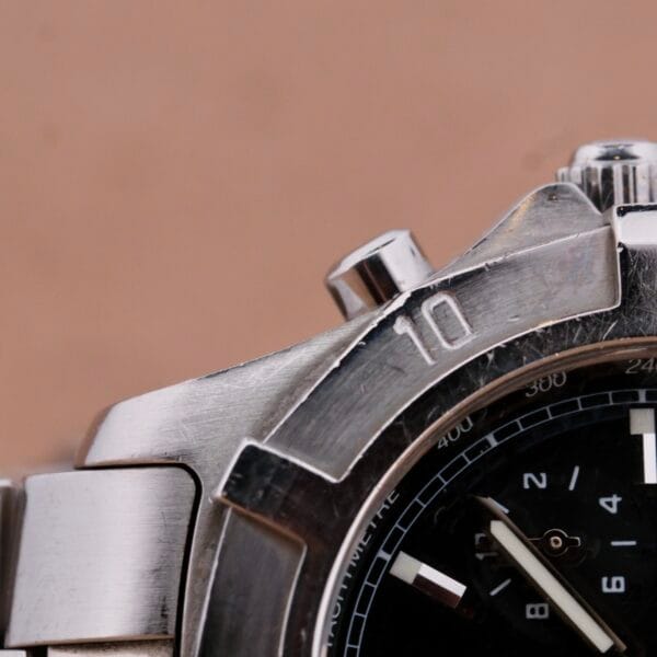 A close-up of a Tag Heuer 2000 Professional Chronograph wristwatch shows a black dial with standout hour markers and hands, plus a rotating numbered bezel. Its metal band elegantly reflects light.