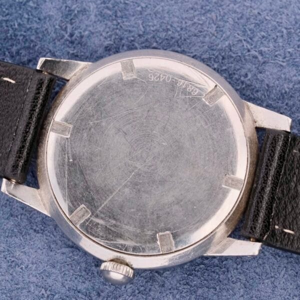 A Girard Perregaux Incabloc Manual Wind wristwatch with a scratched metal back and black leather strap rests on blue fabric. The back features engravings, including 68 and 0426, highlighting its vintage heritage.
