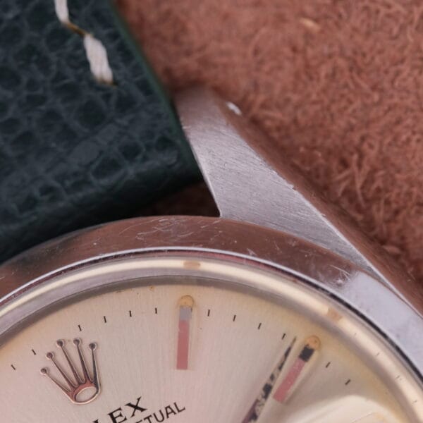 Close-up of the Rolex Oyster Perpetual Date 1500 Silver Dial wristwatch, showcasing the brand logo and PERPETUAL text. It features a metal case and leather strap with stitching against a textured brown background.