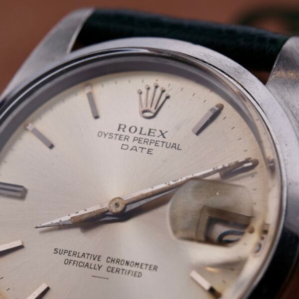 A detailed close-up of the Rolex Oyster Perpetual Date 1500 Silver Dial showcases its elegant silver dial with date function and magnifying lens, enhanced by the signature Rolex logo and Superlative Chronometer Officially Certified text, highlighting its timeless allure.