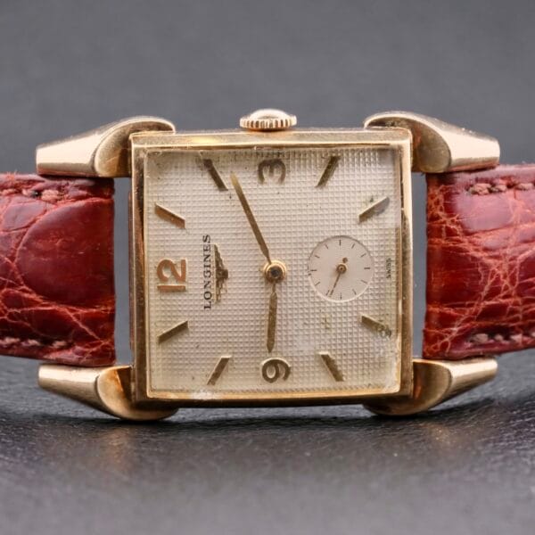 The Longines Franklin Square Waffle Dial Cal 23Z is a vintage watch featuring a textured cream square dial with gold hour markers and hands, a small seconds subdial at 6 oclock, and a brown crocodile-pattern leather strap encased in elegant gold tones.