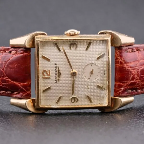 The Longines Franklin Square Waffle Dial Cal 23Z is a vintage watch featuring a textured cream square dial with gold hour markers and hands, a small seconds subdial at 6 oclock, and a brown crocodile-pattern leather strap encased in elegant gold tones.