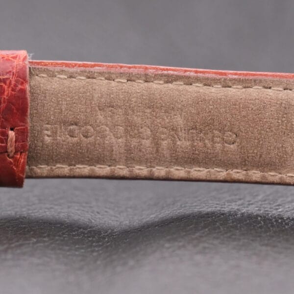 Close-up of a textured red and brown Longines leather strap with faint embossed text on a soft black surface, capturing the elegance of the Longines Franklin Square Waffle Dial Cal 23Z.