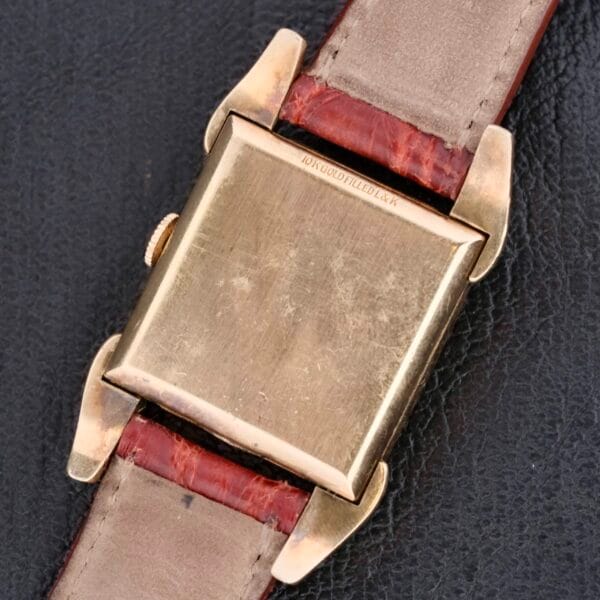 Back view of a Longines Franklin Square Waffle Dial Cal 23Z wristwatch with a gold square face and brown leather strap on a black textured surface, featuring an inscription that is not clearly visible.