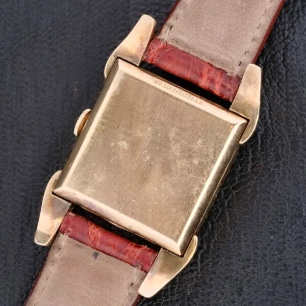 Back view of a Longines Franklin Square Waffle Dial Cal 23Z wristwatch with a gold square face and brown leather strap on a black textured surface, featuring an inscription that is not clearly visible.