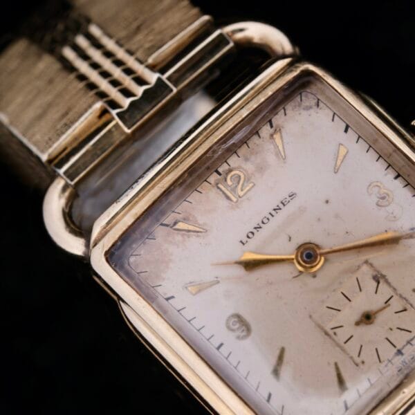 Close-up of a vintage Longines Square Driver Lugs Cal 10L with a gold-toned rectangular case, cream dial, gold hour markers, subdial, and distressed strap against a dark background.
