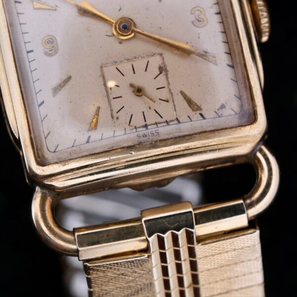 Close-up of a vintage Longines Square Driver Lugs Cal 10L with a gold-tone case and cream dial, featuring gold hour markers and a small seconds subdial at the bottom. The gold-toned strap is enhanced by a textured pattern.