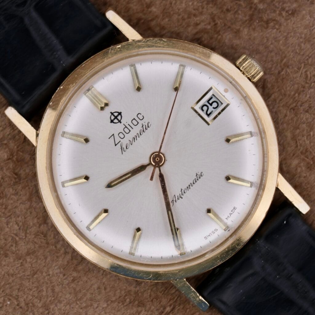 Zodiac Hermetic 14k Gold Automatic Date wristwatch with a white dial, gold markers, and a date window at 3 o’clock.