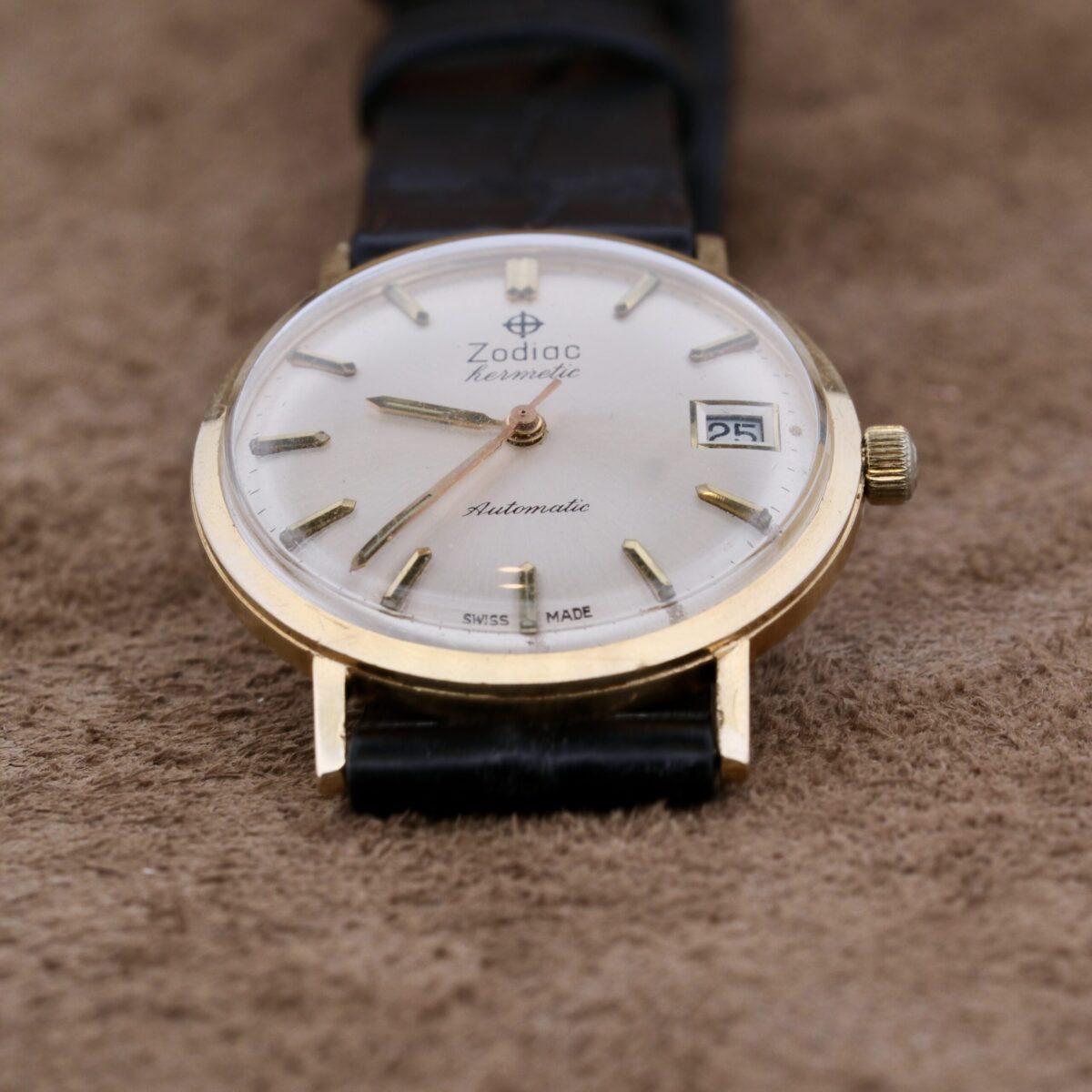 Introducing the Zodiac Hermetic 14k Gold Automatic Date, a timeless masterpiece from Switzerland, crafted between 1960 and 1969. This exquisite timepiece features a 34mm 14k gold case, a sleek silver dial with gold hour markers and hands, central seconds, and a date function. Powered by an automatic movement, it ensures precise timekeeping. The 18mm leather strap offers comfort and security. This watch embodies elegance and functionality, making it a must-have for discerning collectors and enthusiasts.