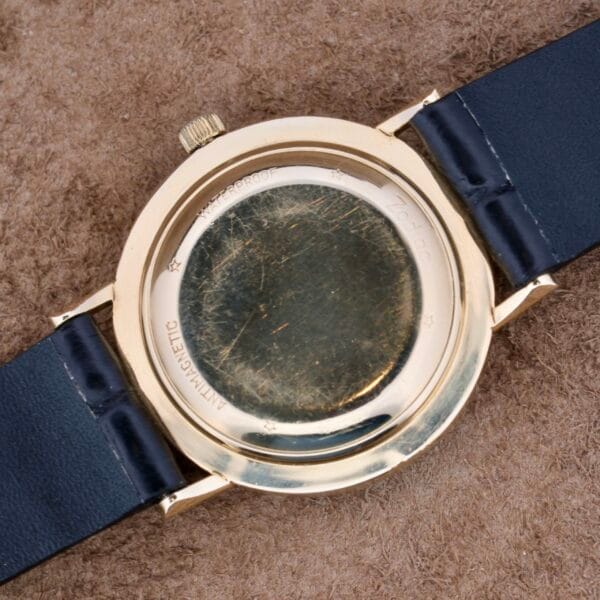 The Zodiac Hermetic 14k Gold Automatic Date watch features an engraved back with WATERPROOF and ANTIMAGNETIC. Its elegant 14k gold case shows wear and scratches, paired with a black leather strap, all set against a textured brown fabric background.