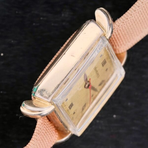 A vintage Longines Square Gilt Dial Central Red Second wristwatch with a rectangular gold case and beige strap, featuring a scratched gilt dial and minimal markings, displayed on a dark textured background.