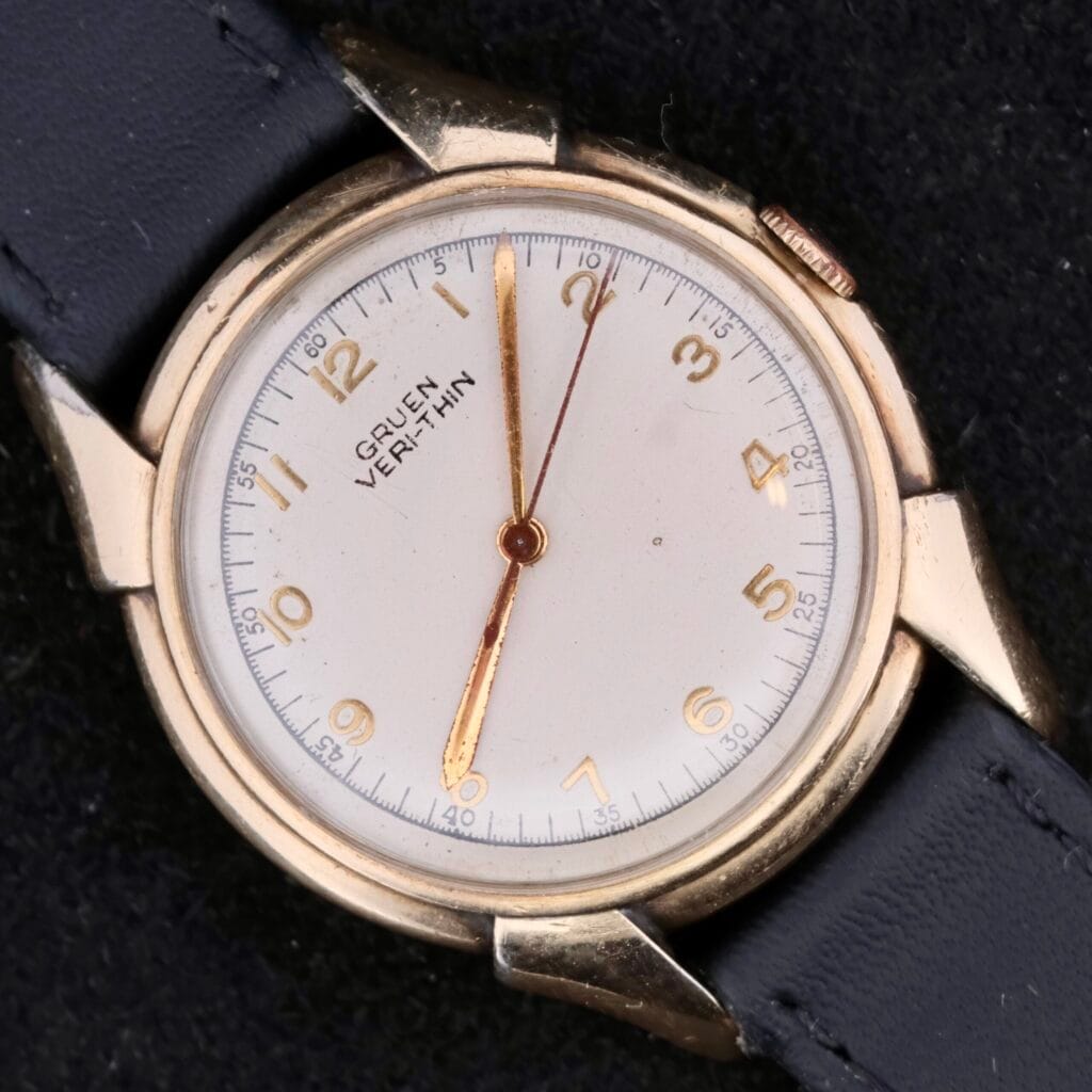 Gruen Veri-Thin Fancy Lugs watch with a white dial, gold markers, and a classic black leather strap.