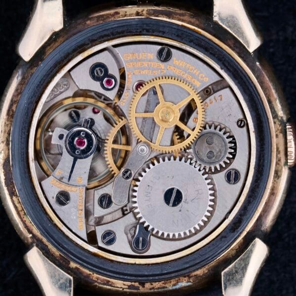 Close-up of a Gruen Veri-Thin Fancy Lugs watch movement with intricate gears and components, including jewels and a balance wheel. Metal parts are meticulously arranged within the circular case, highlighting the detailed craftsmanship of watchmaking.