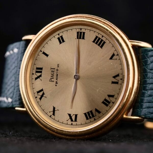 Close-up of a Piaget Quartz 18k Gold Classic watch featuring a gold case with Roman numerals. The timepiece includes a textured dark leather strap, with hands precisely set to about 10:10.