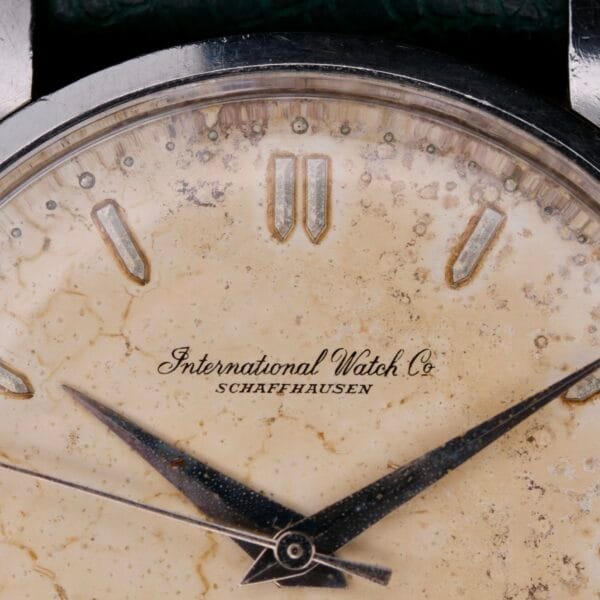 Close-up of an IWC Caltrava Jumbo Cal. 89 Stainless Steel wristwatch face with patina, featuring silver hour and minute hands, triangular hour markers, and the text International Watch Co Schaffhausen, enhancing its classic and vintage look.