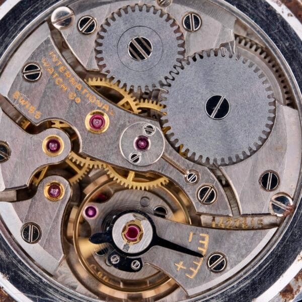 Close-up of a complex watch movement featuring interlocking gears and jewels. The Swiss-made IWC Caltrava Jumbo Cal. 89 Stainless Steel mechanism is intricately detailed with visible markings, showcasing precision engineering.