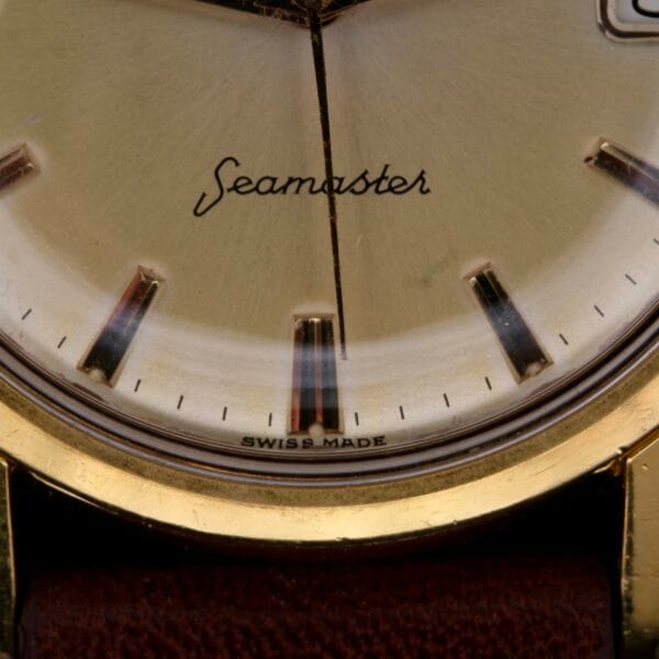 A close-up of the Omega Seamaster Date Automatic Cal 565 watch face prominently displays Seamaster. The brown leather strap accentuates gold details and the Swiss Made marking, with time markers, a hand, and a subtle date display completing this timeless pieces elegance.