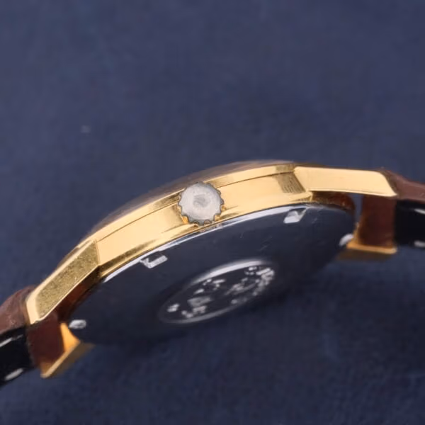 A side view of the Omega Seamaster Date Automatic Cal 565 showcases a gold-toned case, round crown, dark face, and brown leather strap, elegantly set against a dark blue background.