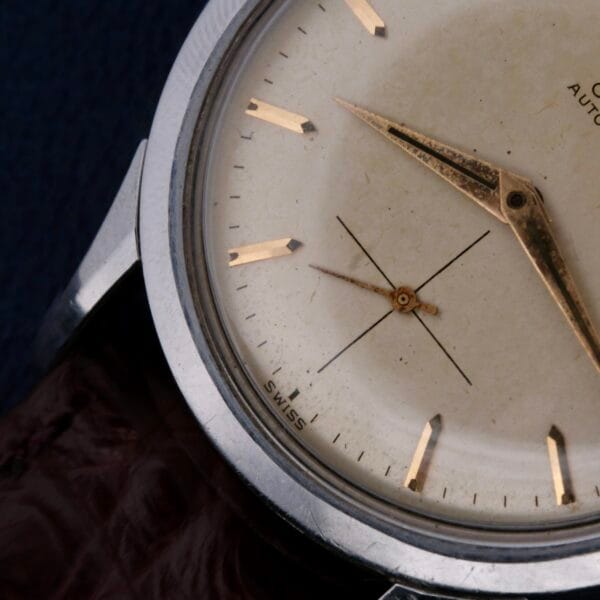 A vintage Omega Automatic Bumper Cal 344 displays an off-white face with gold hour markers and hands, SWISS on the bottom, a brown leather strap, and a stainless steel case.