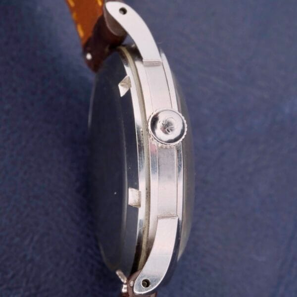 Side view of an Omega Automatic Bumper Cal 344 Stainless Steel Watch with a brown leather strap, elegantly highlighting the crown and its slim profile against a dark blue background.