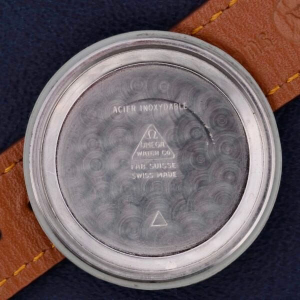 The Omega Automatic Bumper Cal 344 Stainless Steels case back, elegantly textured with a swirl pattern, features engravings: ACIER INOXYDABLE, OMEGA WATCH CO, FAB. SUISSE, and SWISS MADE. It is paired beautifully with a brown leather strap.