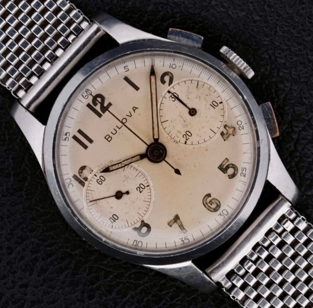 Bulova Chronograph 13AK Valjoux 23 Stainless Steel watch with a mesh band displayed on a black textured surface.