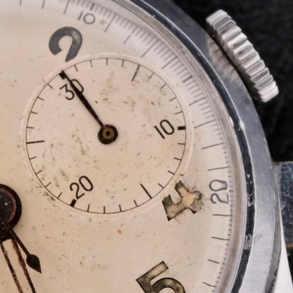 A close-up of the Bulova Chronograph 13AK Valjoux 23 watch face reveals its vintage charm. The weathered dial features a small seconds sub-dial at 9 oclock and visible scratches, while elegant hands point between 2 and 3. Its timeless look is completed by bold black numbers.