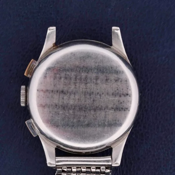 The image displays the back of a Bulova Chronograph 13AK Valjoux 23 Stainless Steel wristwatch with a metallic strap, set against a dark blue textured surface. The watch, featuring two side buttons, shows wear with scratches visible on its back.