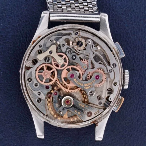 The close-up view of the Bulova Chronograph 13AK Valjoux 23 Stainless Steel showcases intricate gears, springs, and elements in silver and copper tones. The open back reveals the meticulous craftsmanship and engineering excellence of its internal parts.