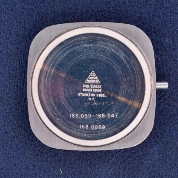The Omega Constellation TV Case Certified Chronometer watch case back sits on a dark fabric, highlighting engravings like OMEGA, Swiss Made, and the numbers 166.059-168.047 and 168.0059.