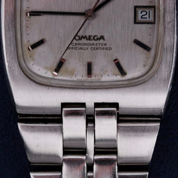 A close-up of the Omega Constellation TV Case Certified Chronometer wristwatch reveals its silver rectangular case, metal link bracelet, date window at 3 oclock, and the text Omega Chronometer Officially Certified displayed on the dial.