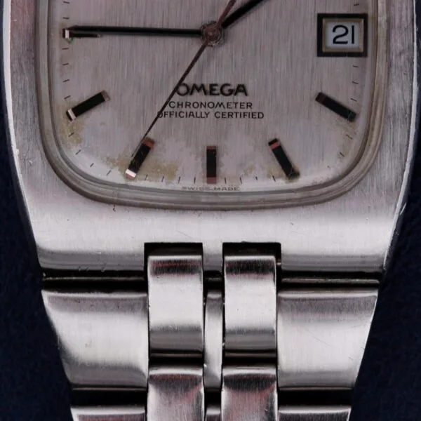 A close-up of the Omega Constellation TV Case Certified Chronometer wristwatch reveals its silver rectangular case, metal link bracelet, date window at 3 oclock, and the text Omega Chronometer Officially Certified displayed on the dial.