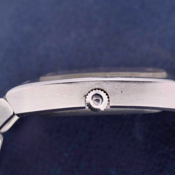 Close-up of the Omega Constellation TV Case Certified Chronometer, showcasing its silver elegance with a round, textured winder. The dark, slightly textured background amplifies the luxury of this exquisite timepiece.