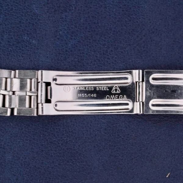 An Omega Constellation TV Case Certified Chronometer stainless steel watch bracelet lies on a dark blue textured surface, with the open clasp showing engravings of Stainless Steel, 1155/146, and the Omega logo.