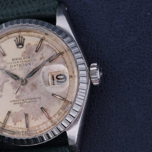 The Rolex Datejust 1603 Pie-Pan Dial watch features a fluted bezel, date display set to the 10th, weathered dial, and dark green textured strap against a dark background, emphasizing its timeless elegance.