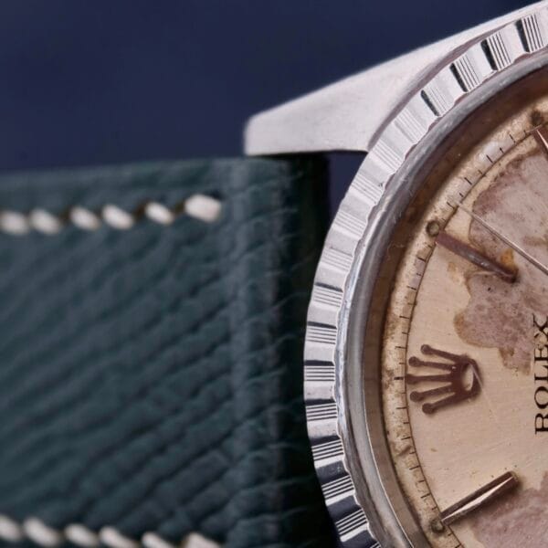 Close-up of a worn vintage Rolex Datejust 1603 Pie-Pan Dial watch face, featuring a leather strap with visible stitching. The aging watch face has patina, tarnishing, and Roman numeral hour markers.