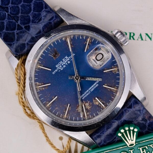 The Rolex Oyster Perpetual Date 1500 features a vintage blue, weathered dial with a date window, silver hands, and indices. It includes a blue leather strap and iconic crown logo, elegantly paired with an authentic Rolex certificate.