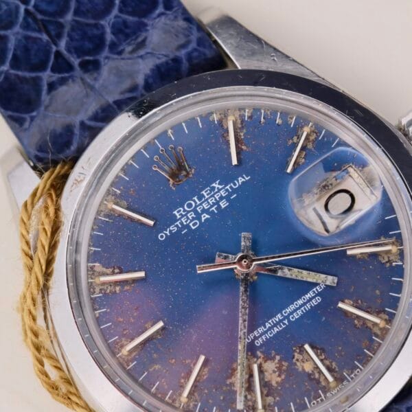 Close-up of a vintage Rolex Oyster Perpetual Date 1500 with a faded blue dial, showcasing signs of aging. Prominent silver hour markers and hands stand out. This classic timepiece includes a textured blue strap subtly tied with a thin rope.