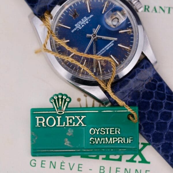 Displayed on a box is the Rolex Oyster Perpetual Date 1500 Blue Dial watch, featuring a blue face and strap, accompanied by a green tag labeled Oyster Swimpruf.