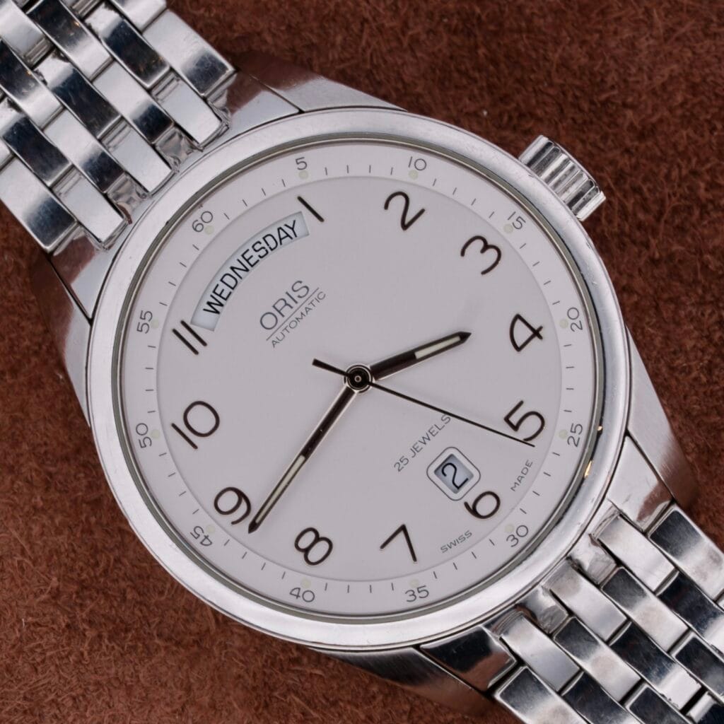 The Oris XXL Full Day Automatic wristwatch, shown displaying Wednesday and the date 2, rests on a brown textured surface.