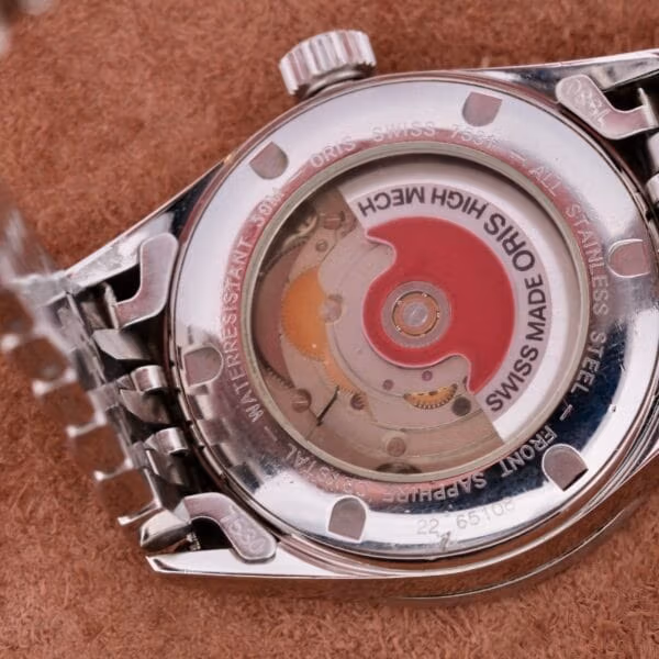 The Oris XXL Full Day Automatic flaunts Swiss-made precision with an engraved silver casing, stainless steel durability, and water resistance. Its intricate inner movement is visible through the back, highlighting gears and a striking red rotor. An elegant metal bracelet completes the design.