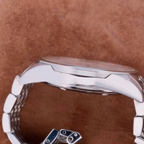 Side view of an Oris XXL Full Day Automatic wristwatch with a silver metal link band on a brown textured background, highlighting its thickness and design details.