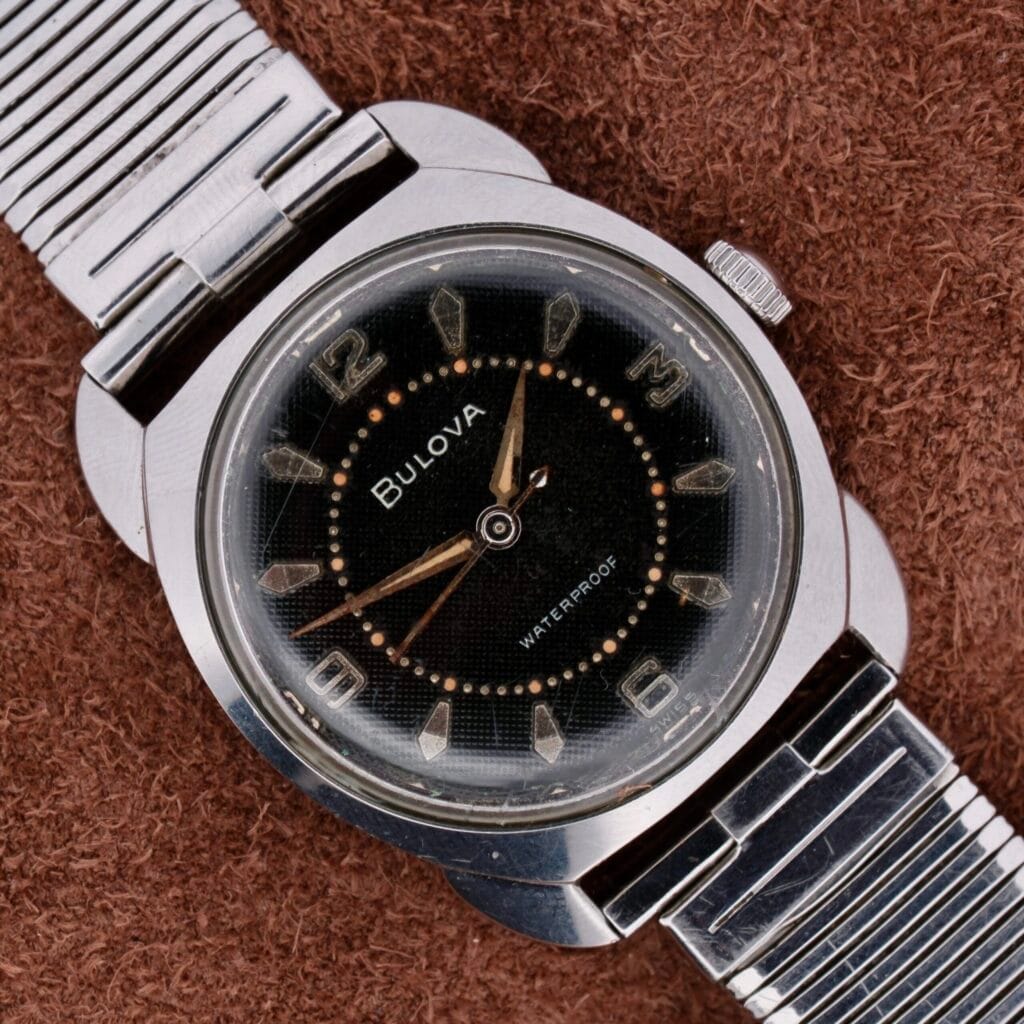 A Bulova Seabee Charcoal Waffle Dial wristwatch with a silver band, displayed on a brown textured surface.