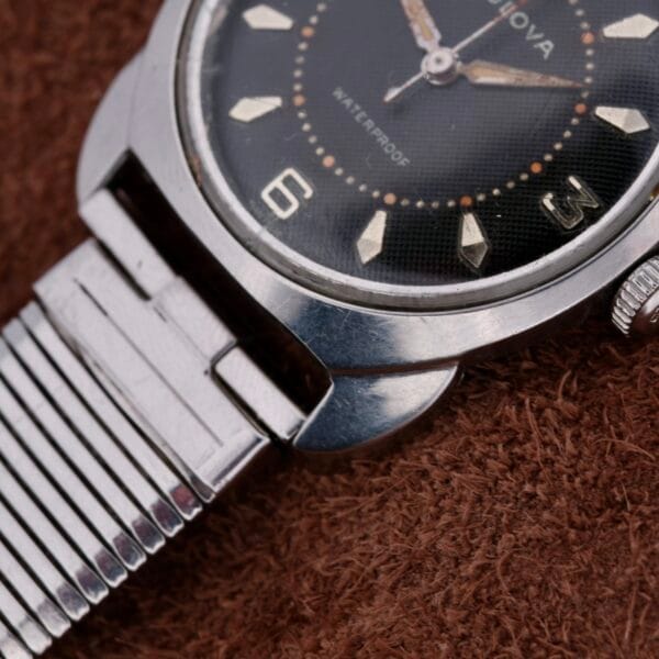 Close-up of the Bulova Seabee Charcoal Waffle Dial wristwatch, showcasing its charcoal waffle dial with silver markers and a metal bracelet on a brown textured surface. WATERPROOF is prominently displayed on the watch face.