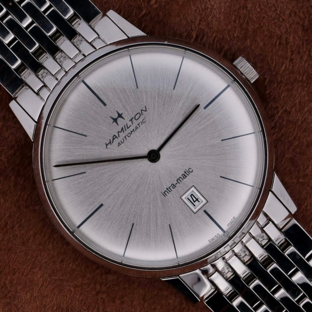 Hamilton Intramatic Date Stainless Steel wristwatch with date display, shown on a brown textured background.