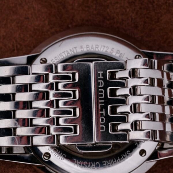 Close-up of a Hamilton Intramatic Date Stainless Steel watch back with a silver band, featuring HAMILTON engraved on it. The watch details water resistance of 5 bar (72.5 PSI) and showcases SWISS and SAPPHIRE CRYSTAL marking its refined case.